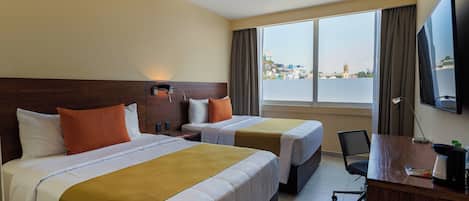 Habitación de hotel con dos camas, un escritorio, una silla, un televisor y un ventanal con vistas a la ciudad.