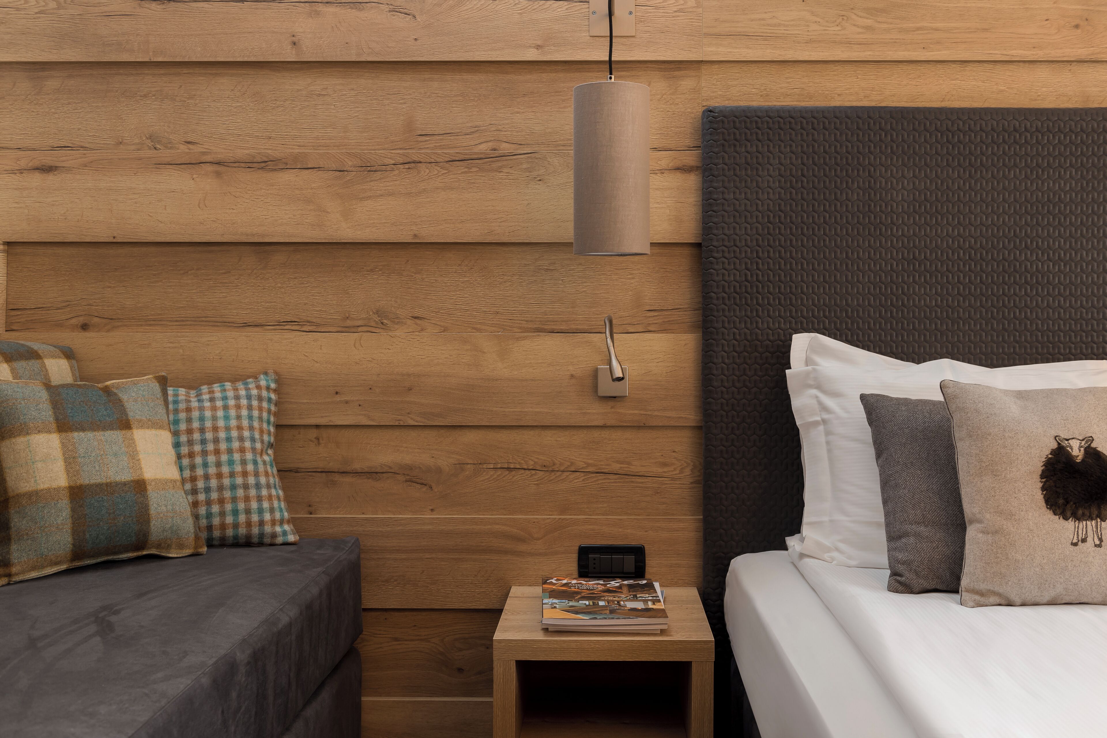 Una camera da letto con parete in legno, un divano grigio, un comodino con una lampada e un letto con cuscini.