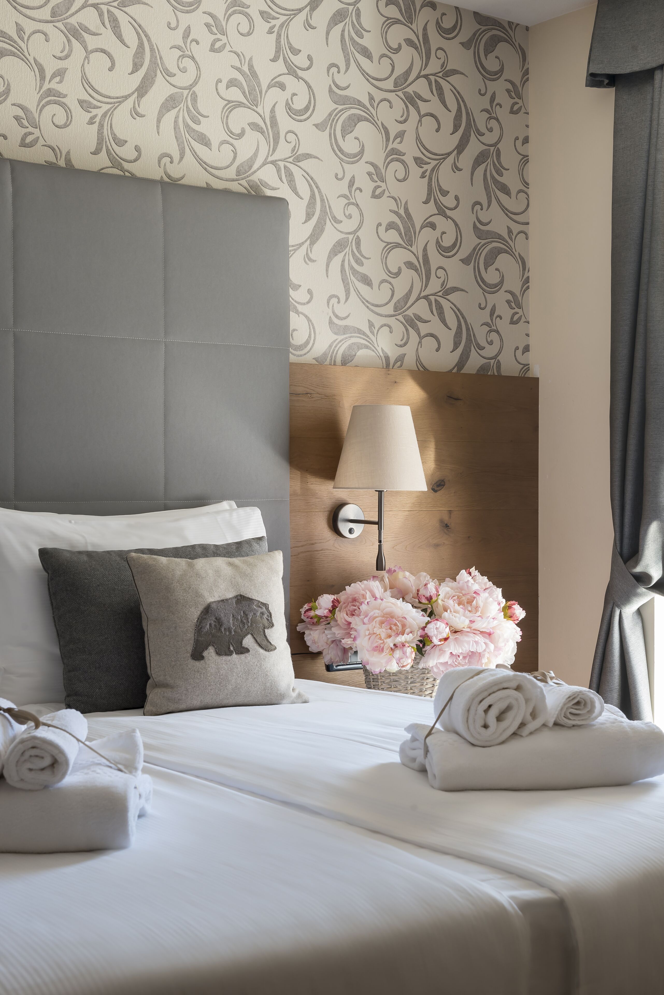 A hotel room with a neatly made bed, a lamp, and a vase of flowers.