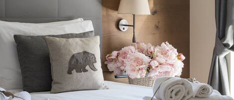 A hotel room with a neatly made bed, a lamp, and a vase of flowers.