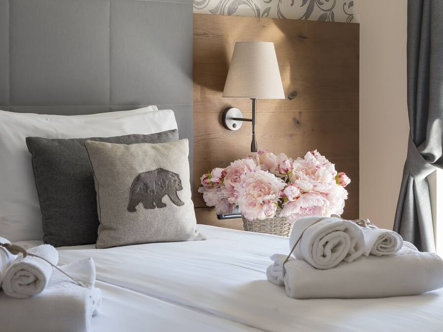 A hotel room with a neatly made bed, a lamp, and a vase of flowers.