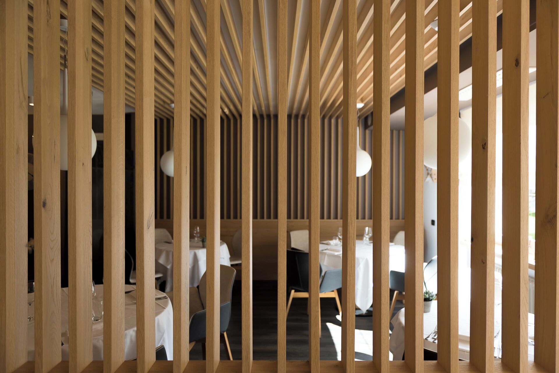 Un interno moderno caratterizzato da pannelli in legno verticali, tavoli con tovaglie bianche e sedie.