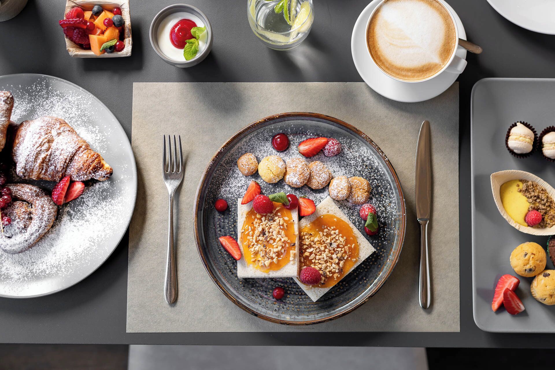 Ein Frühstückstisch mit Croissants, Obst, Gebäck und einer Tasse Kaffee.
