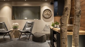 A modern lounge area with a round wooden table, two chairs, a sofa, and a large wall clock.