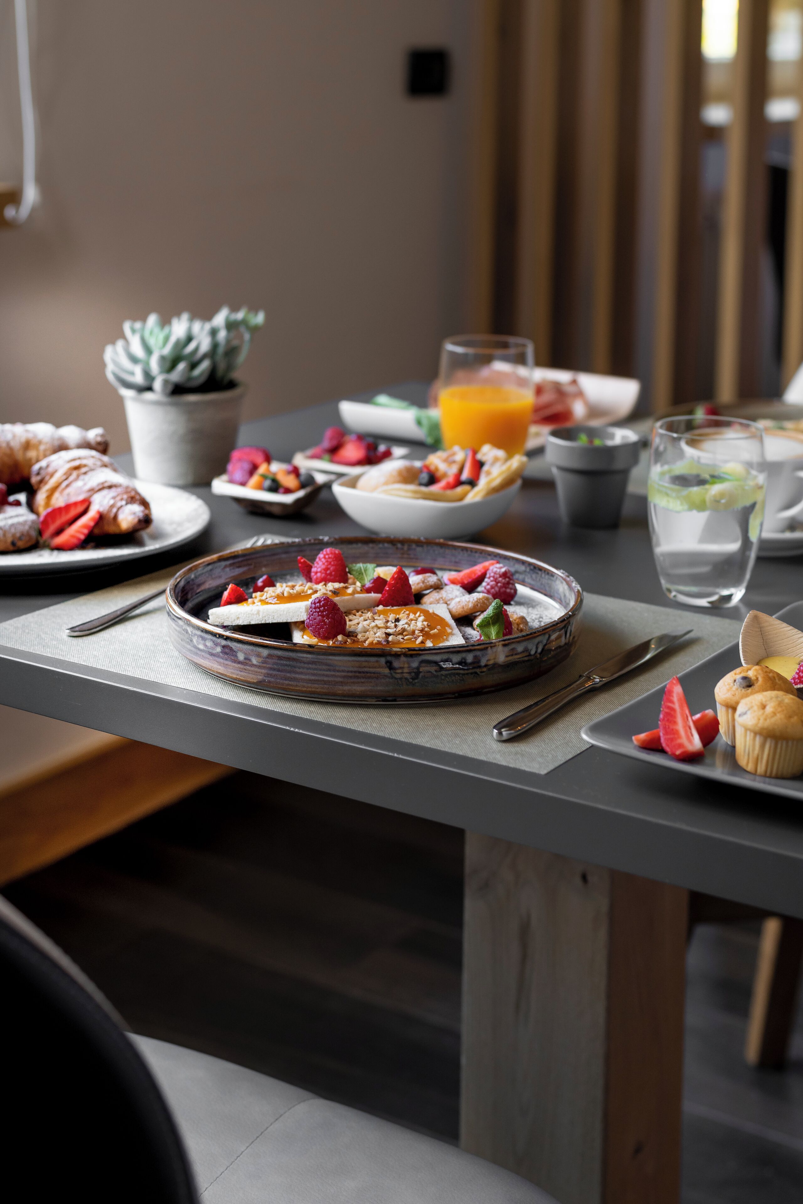 Una mesa de desayuno con cruasanes, fruta y un tazón de cereal.