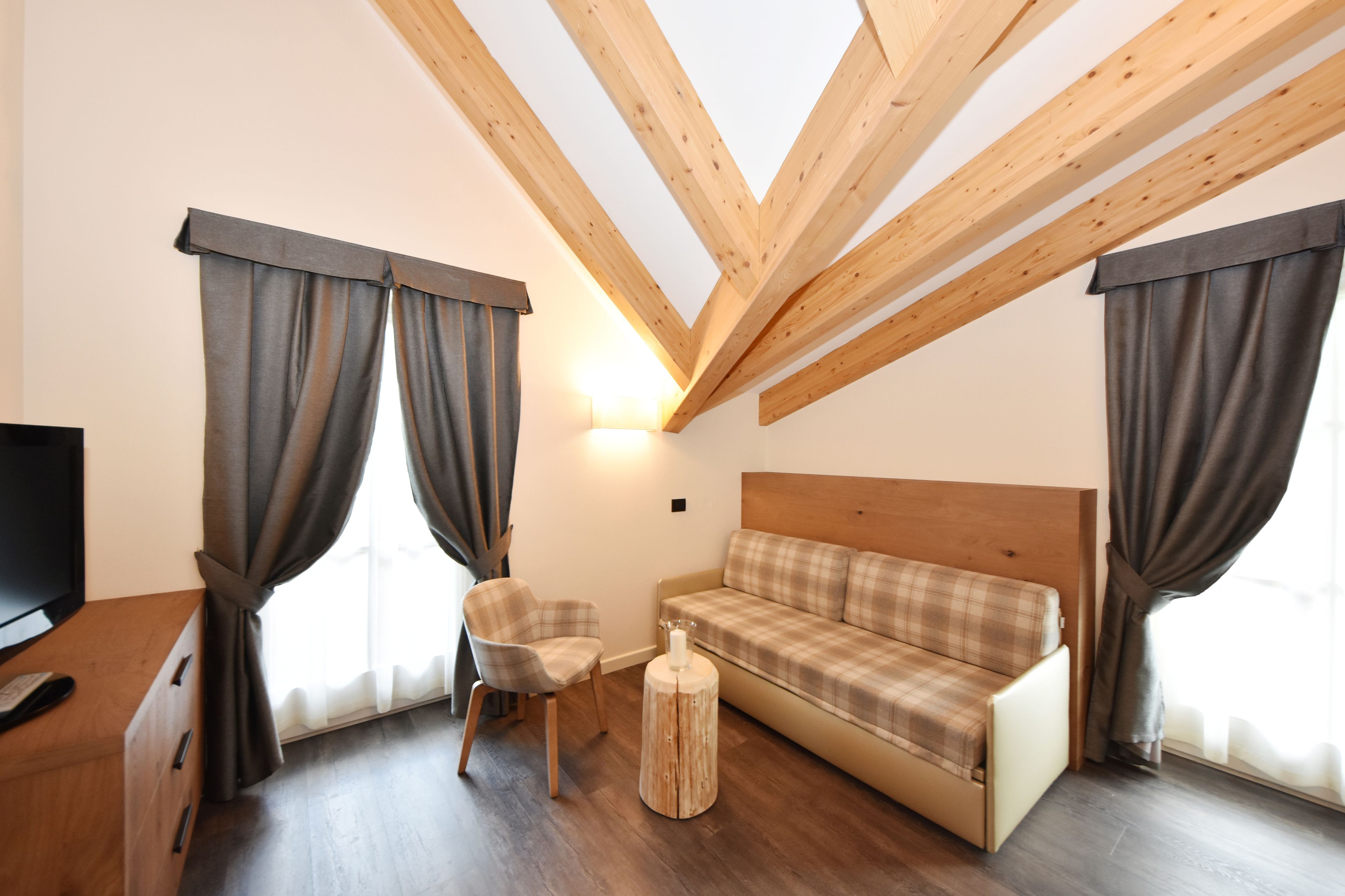 A modern room with a wooden ceiling, a sofa, a chair, a small round table, and a TV.