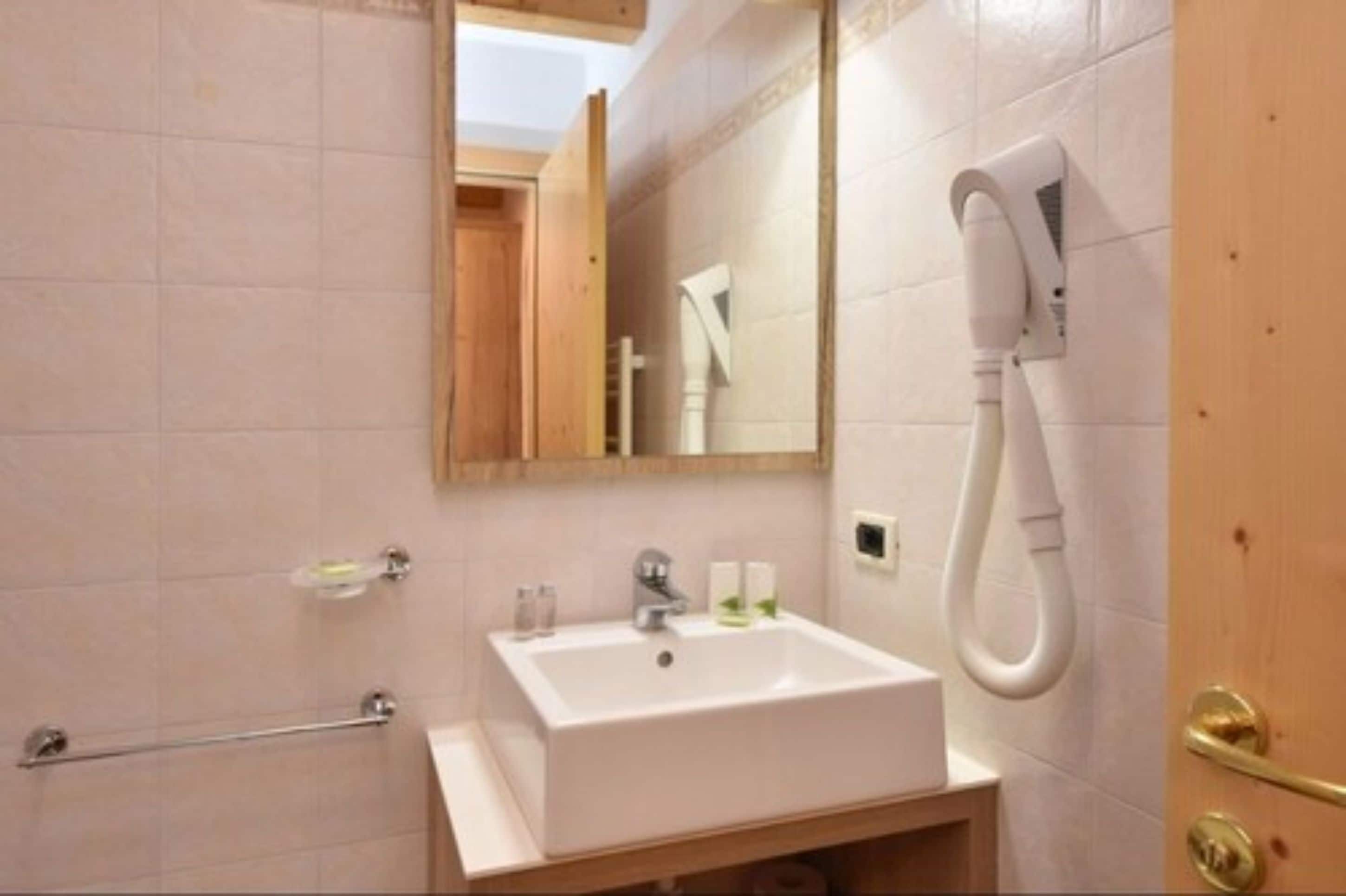 A bathroom with a white sink, a towel rack, a mirror, and a hairdryer mounted on the wall.