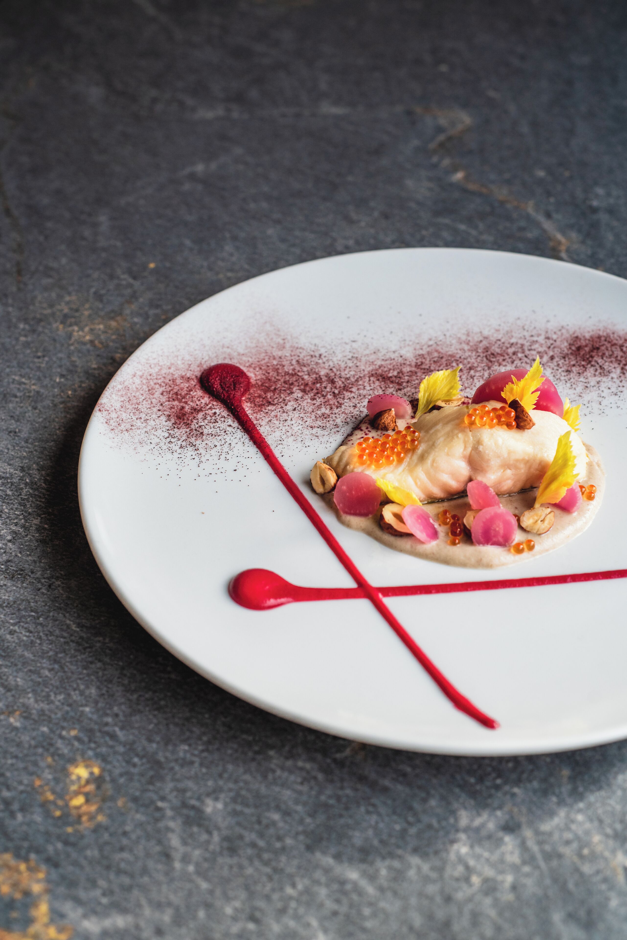 Un piatto bianco con un dessert a base di pesce, frutti di bosco e caviale.
