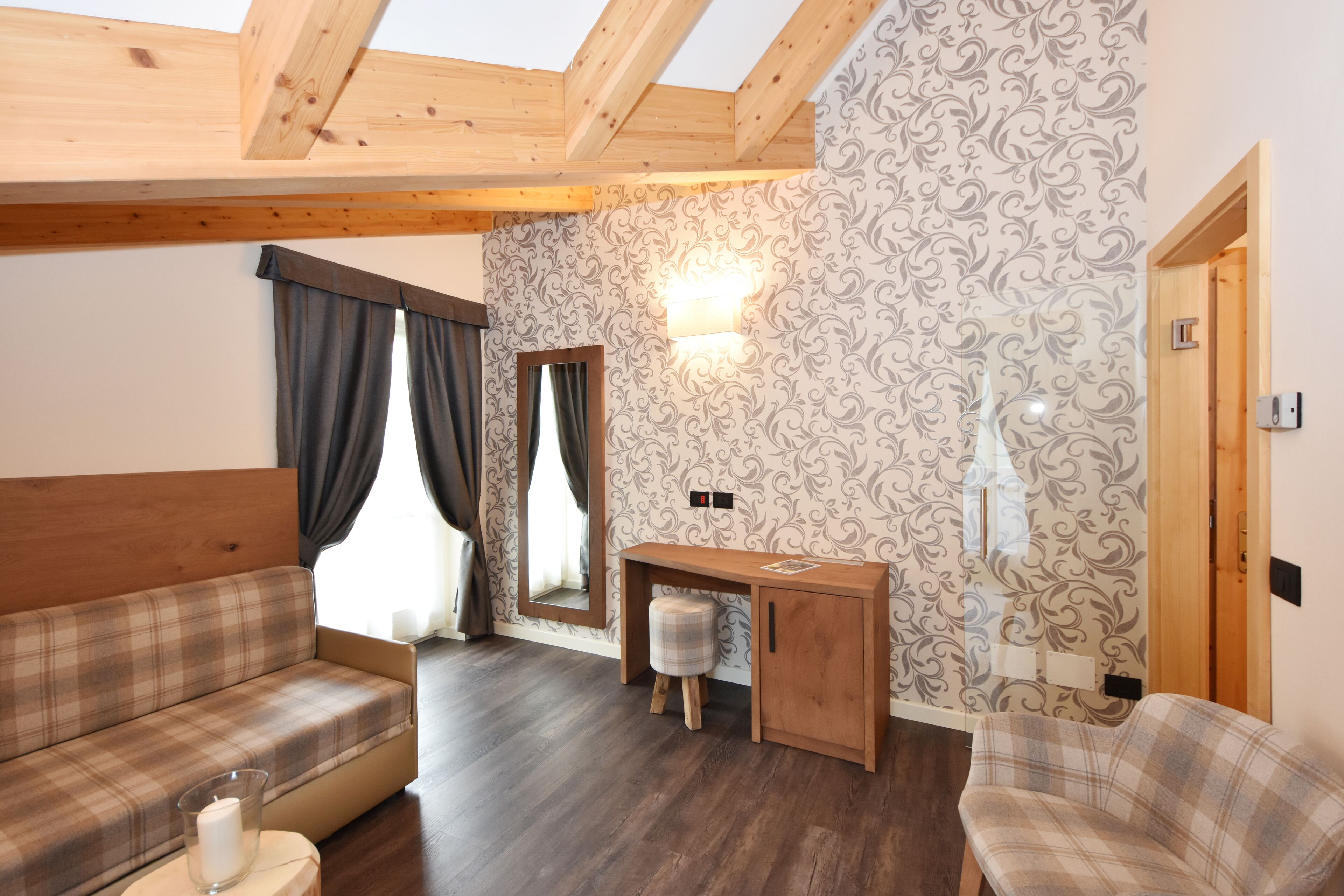 Una habitación acogedora con techo de madera, un sofá a cuadros, un escritorio pequeño con taburete y papel tapiz estampado.