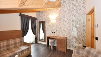 Ein gemütliches Zimmer mit Holzbalkendecke, einem Karosobensofa, einem kleinen Schreibtisch mit Hocker und Wandpapier mit Muster.