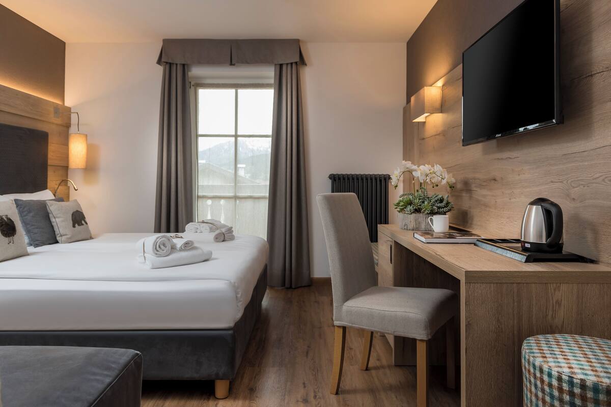 A hotel room with a bed, a desk, a chair, a TV, and a window with curtains.