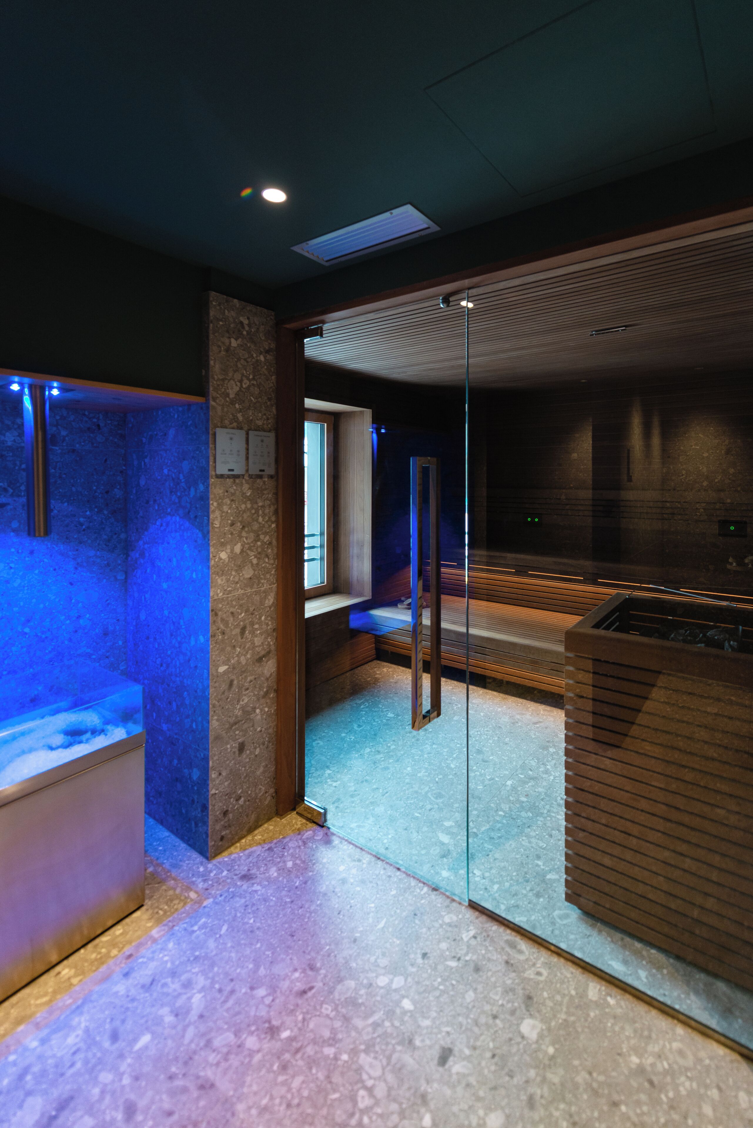 A modern spa room with a glass partition, a heated floor, and a wooden bench.