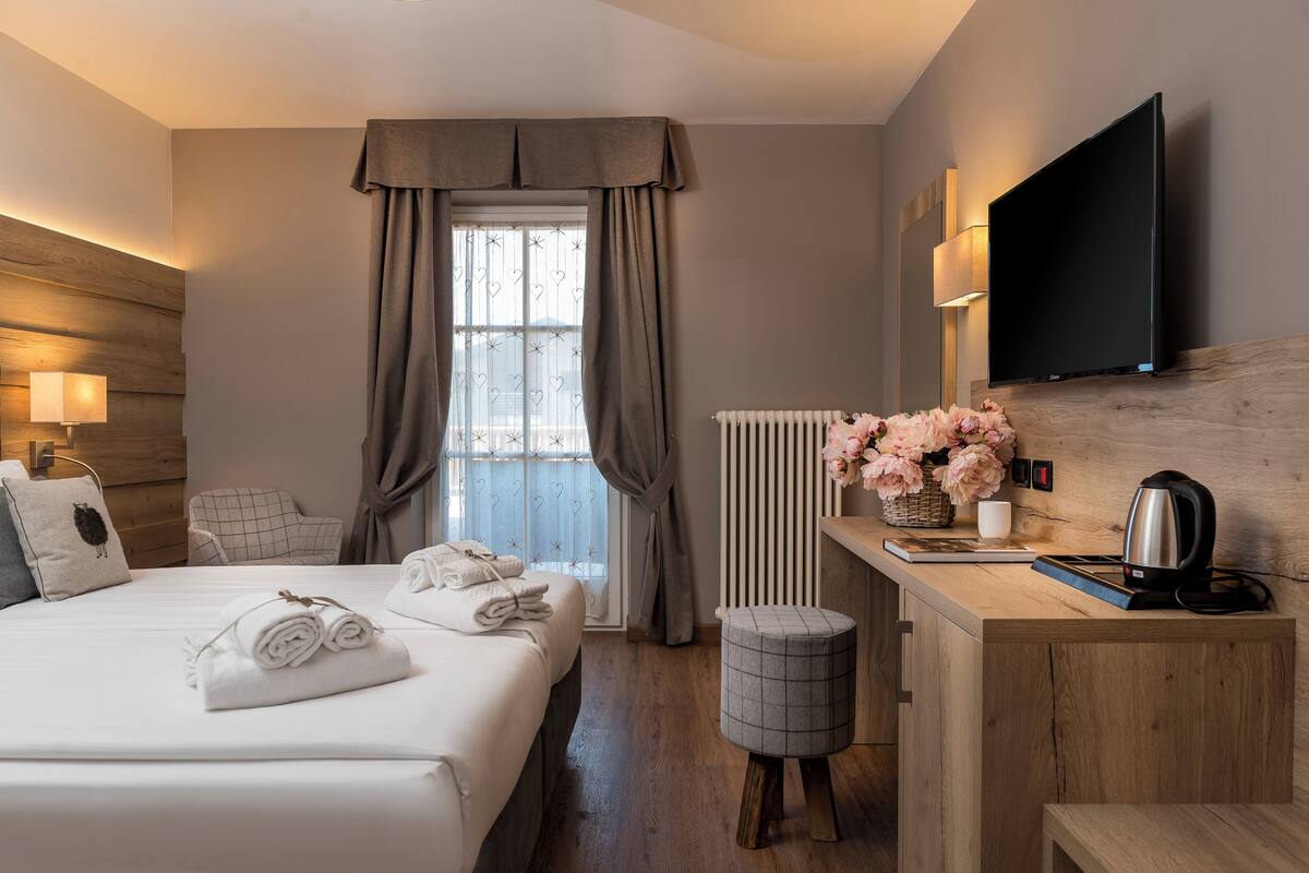 A hotel room with a bed, a desk, a TV, a radiator, and a window with curtains.
