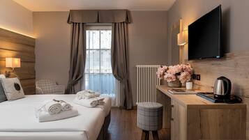 A hotel room with a bed, a desk, a TV, a radiator, and a window with curtains.