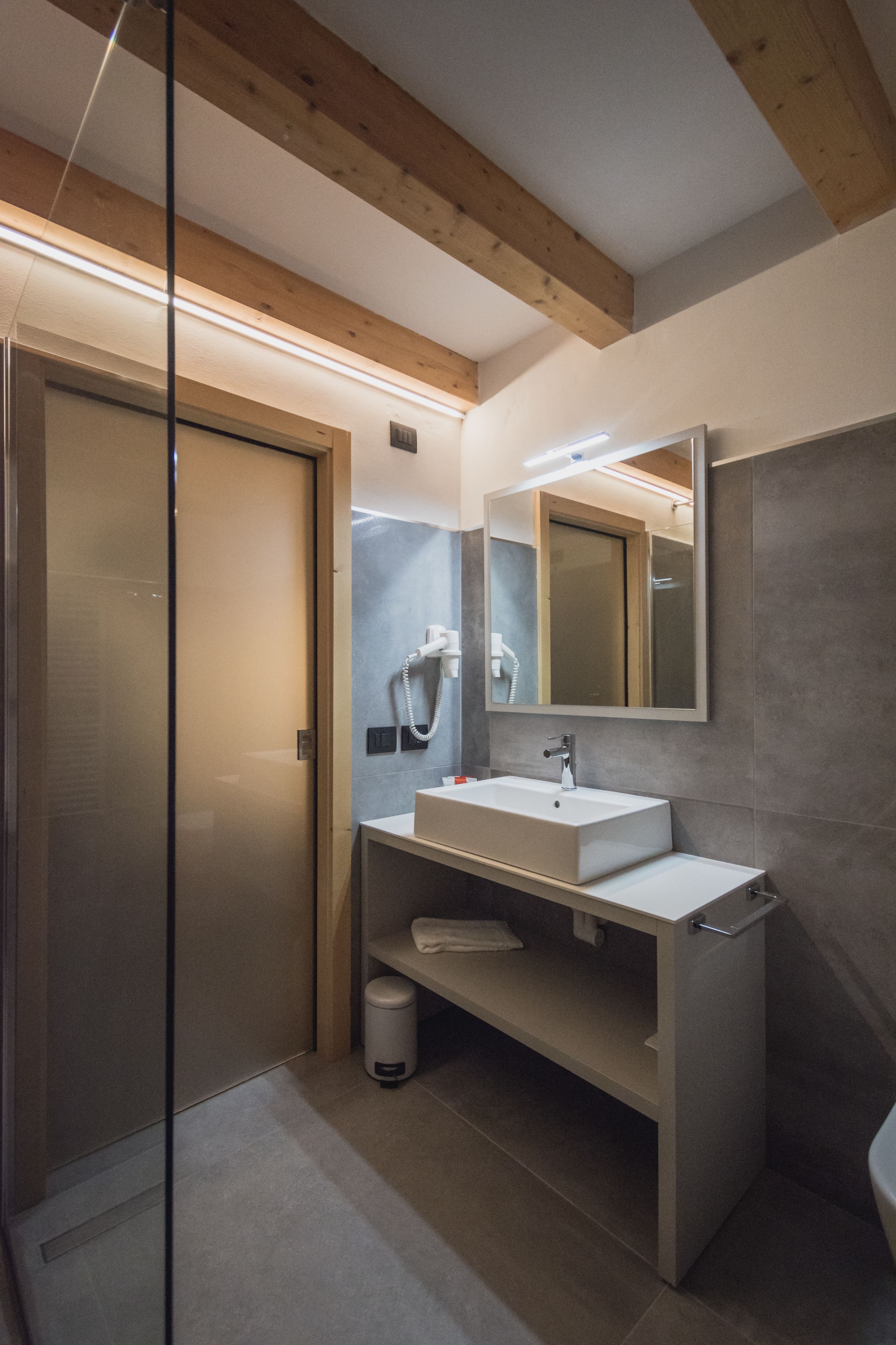 A modern bathroom with a glass shower enclosure, a white sink, and a large mirror.