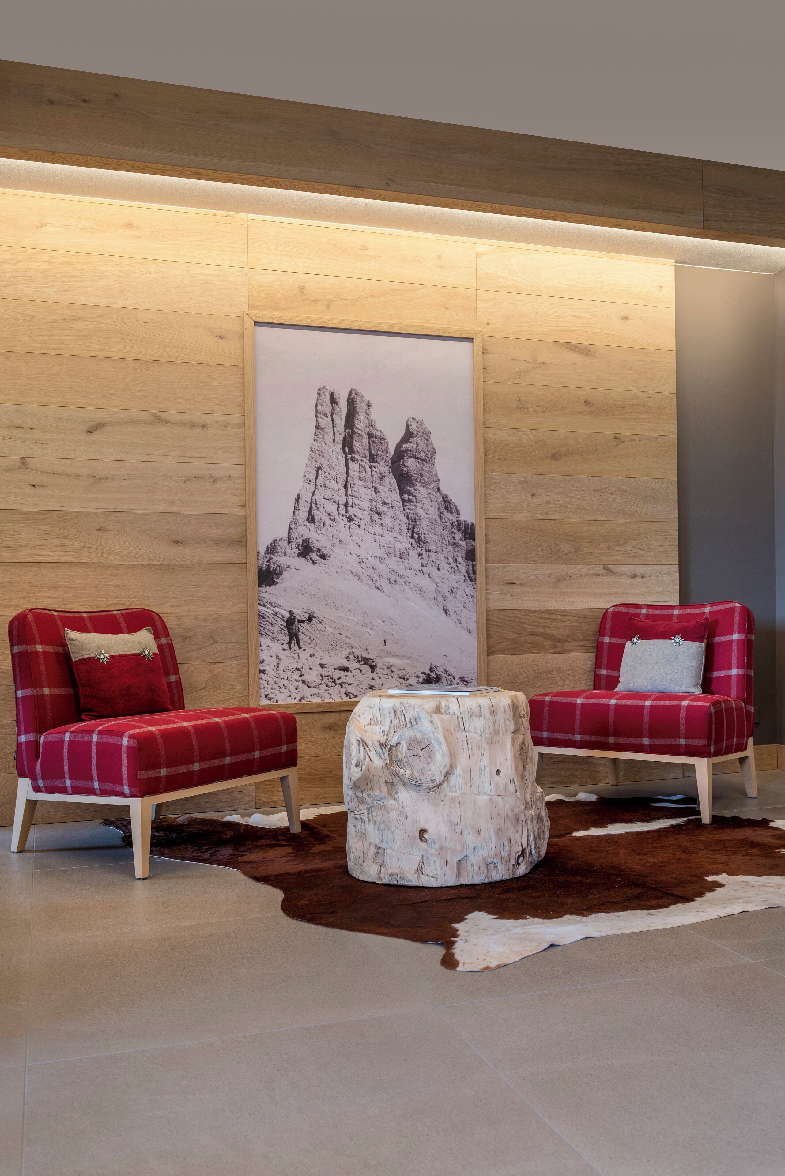 Una habitación moderna con dos sillones rojos con estampado de cuadros, una pared de madera y una fotografía grande de una montaña.