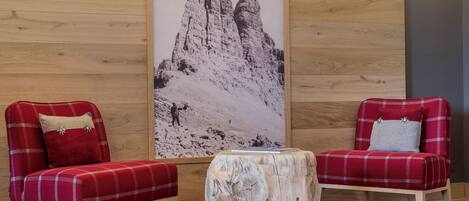 Una habitación moderna con dos sillones rojos con estampado de cuadros, una pared de madera y una fotografía grande de una montaña.
