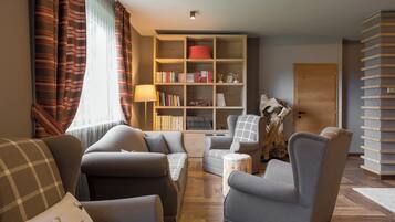 Uma sala de estar acolhedora com um sofá, poltronas, uma estante e uma luminária.