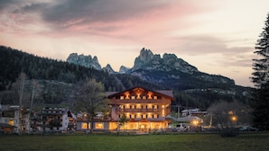 A large, multi-story hotel with a prominent balcony, set against a mountainous backdrop.