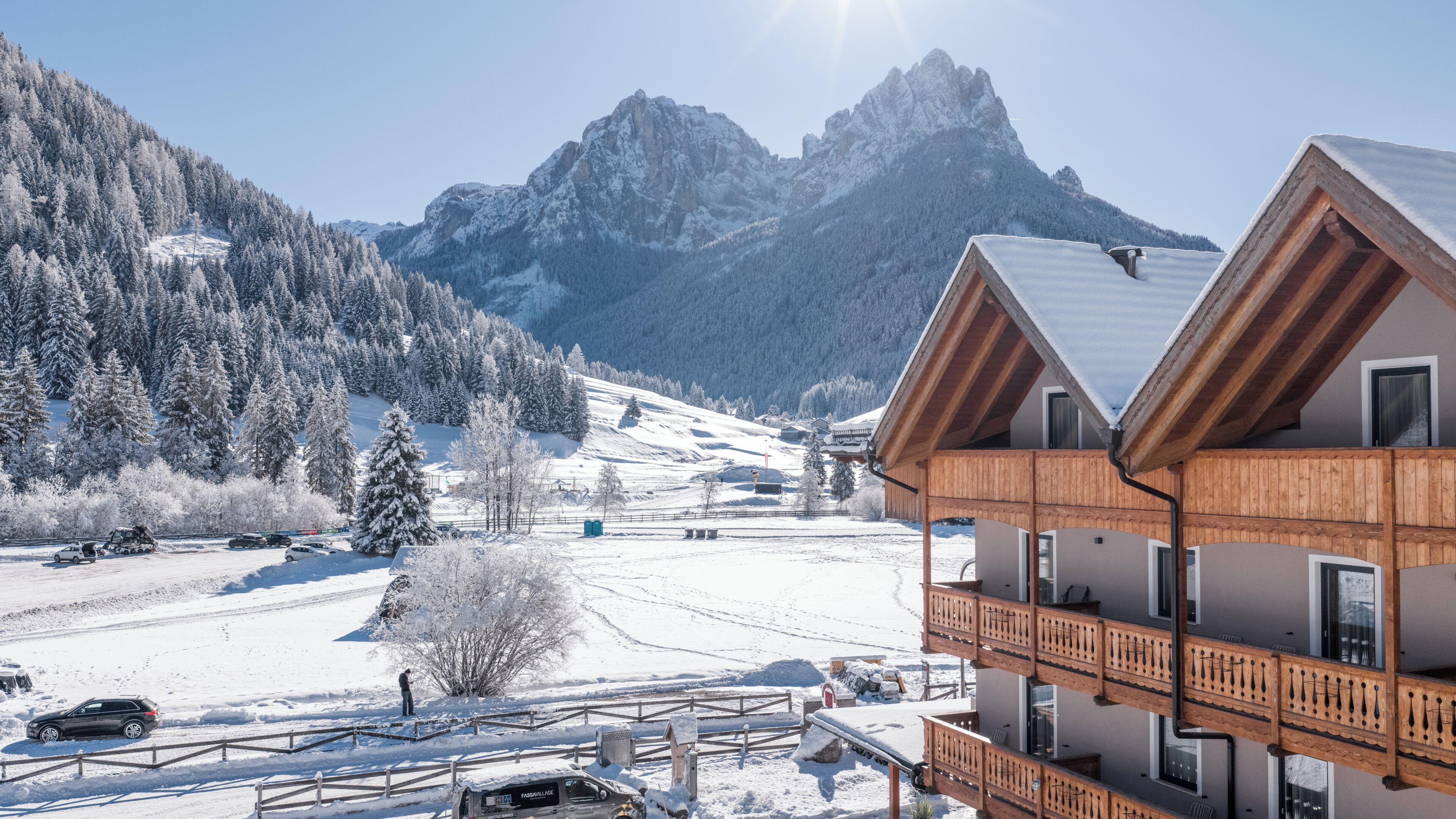 Un albergue de montaña con fachada de madera, varios balcones y vistas a laderas nevadas y montañas.