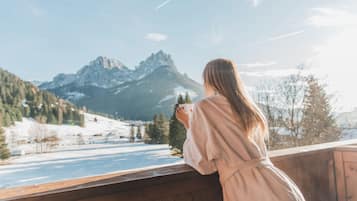Una persona parada junto a un balcón de madera con vistas a un paisaje montañoso, con laderas nevadas y árboles.