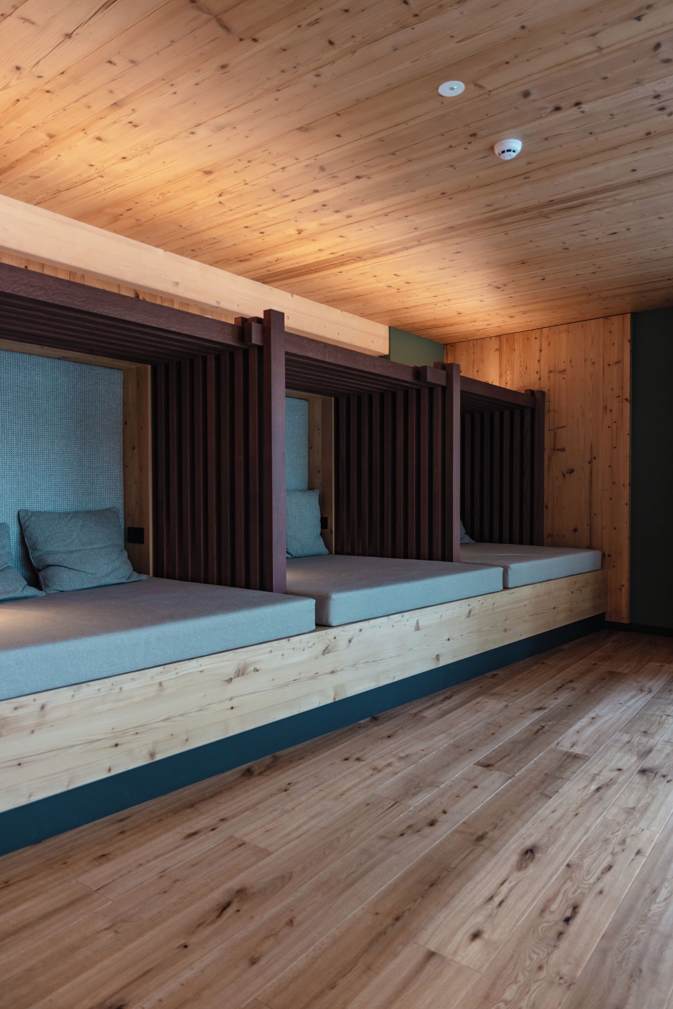 A room with a sloped ceiling and wooden beams, featuring a built-in bench with cushions and a mattress.