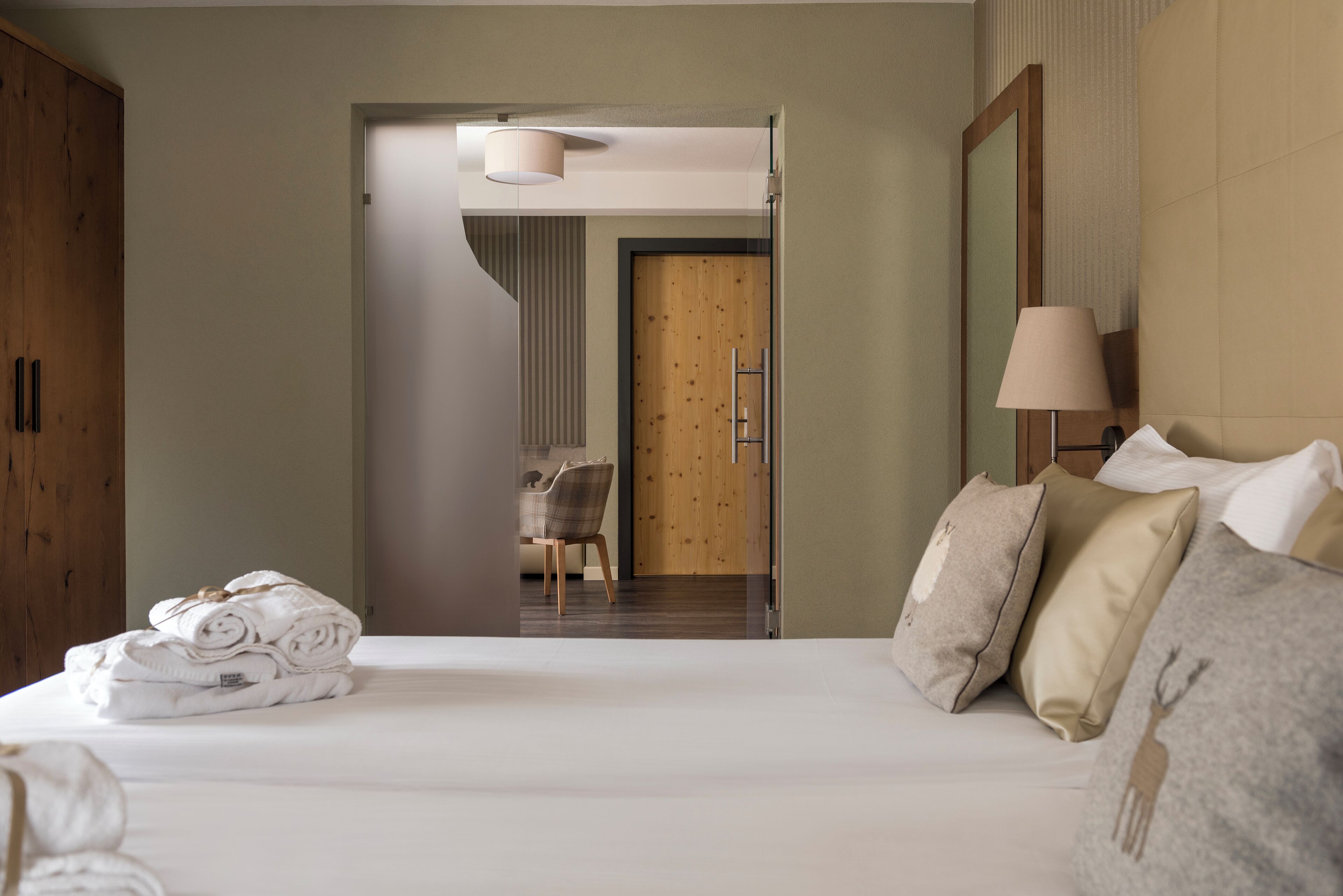 Une chambre d’hôtel avec un lit bien fait, une armoire en bois, une chaise et un bureau avec une lampe.