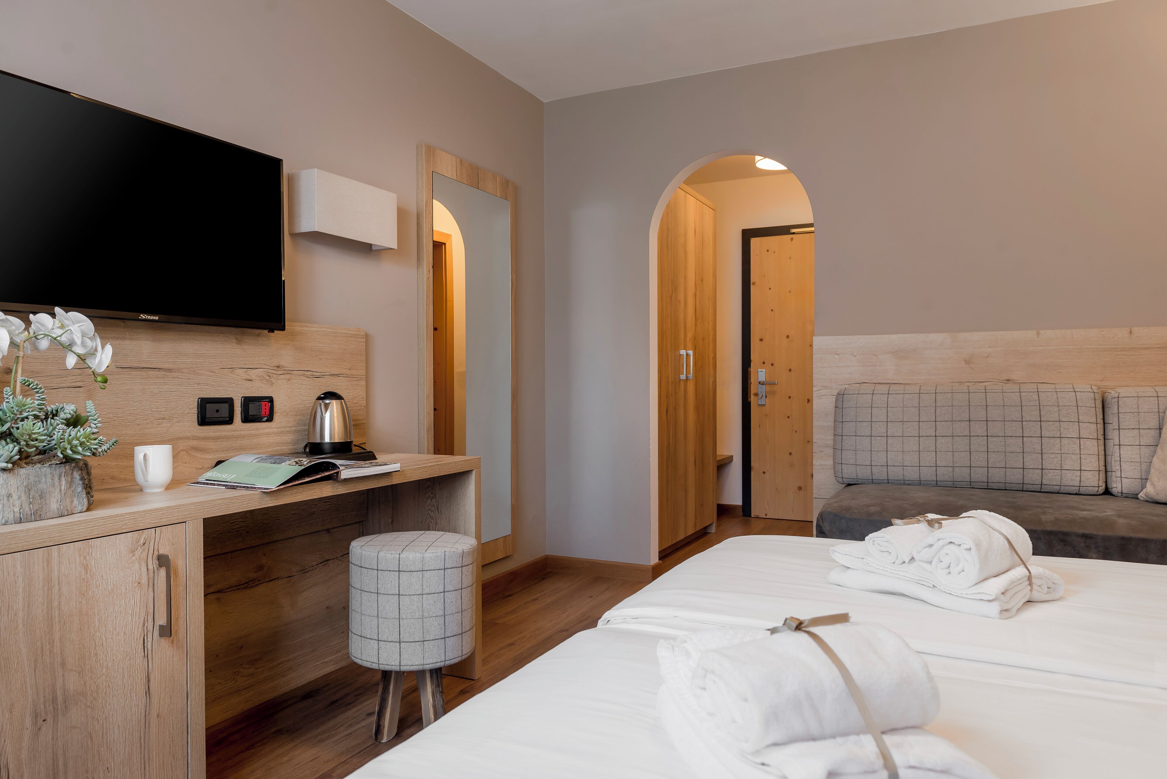 Une chambre d’hôtel comprenant un lit, un bureau, une télévision, un miroir, un petit tabouret et un canapé.