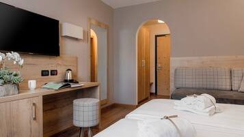 Quarto de hotel com cama, escrivaninha, televisão, espelho, um banquinho pequeno e um sofá.