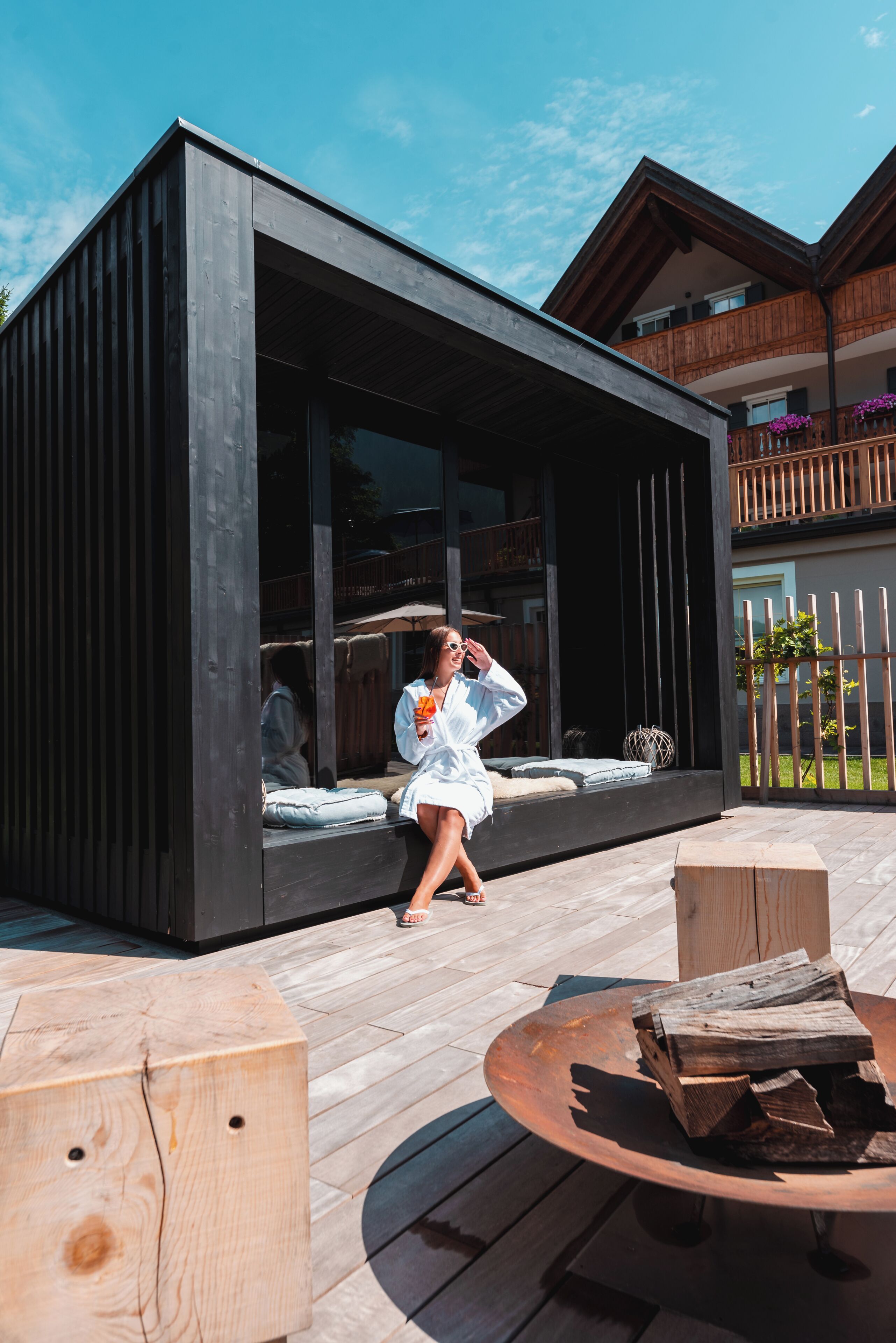 Un área de estar moderna al aire libre con una terraza de madera, una mesa redonda y un banco empotrado con cojines.