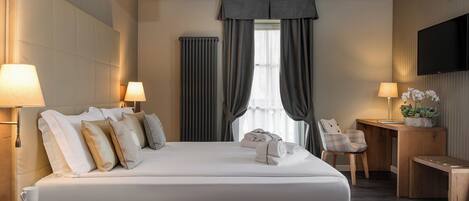 A hotel room with a large bed, bedside lamps, a small table with a plant, and a TV on the wall.