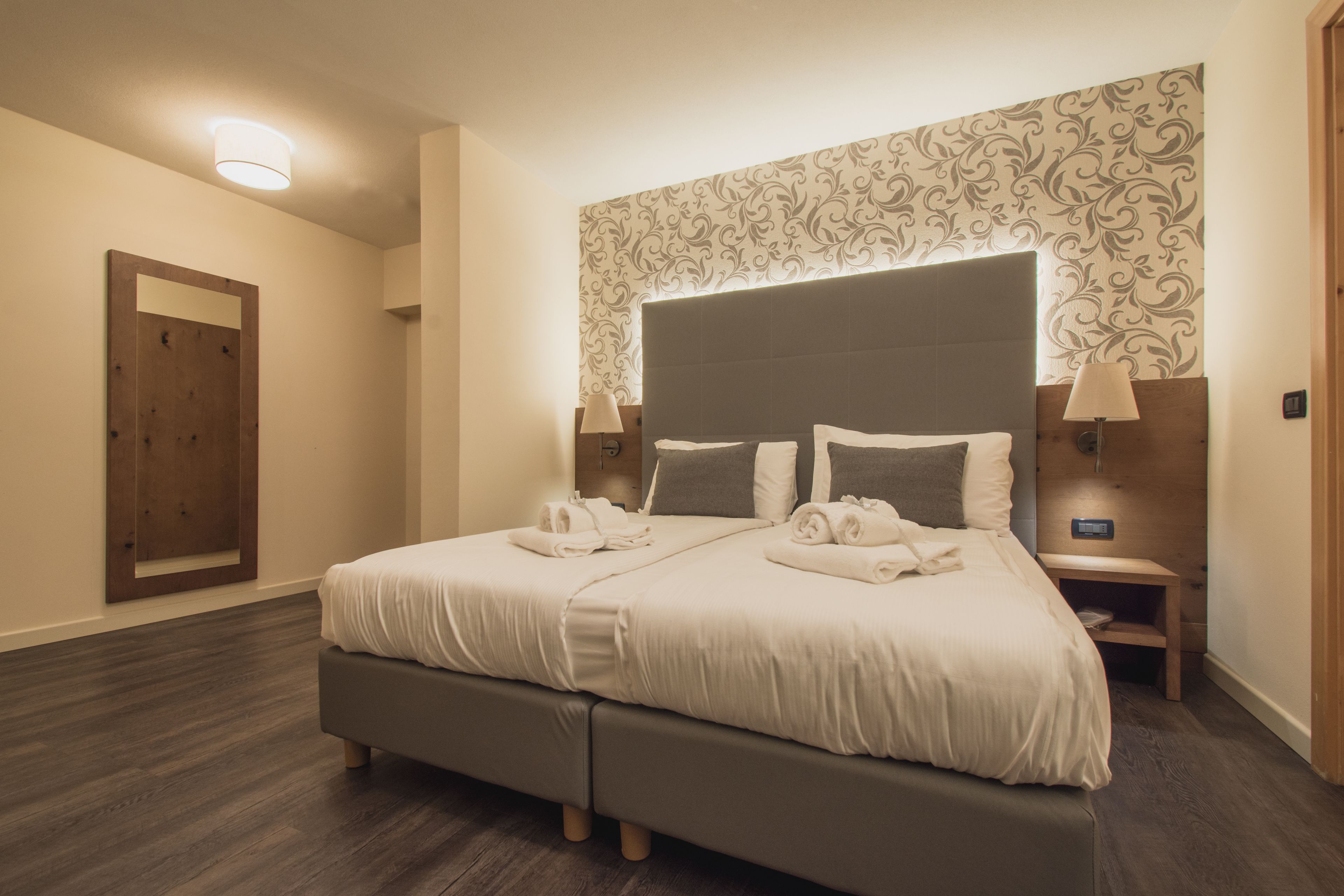 A double bed with a headboard, bedside tables with lamps, a wooden door, and a patterned wallpaper.