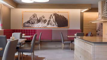 Um restaurante com teto de madeira alto, uma grande pintura de montanha na parede, paredes com padrão xadrez vermelho e branco e um tapete de couro de vaca no chão.