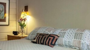 Una cama bien hecha con ropa de cama estampada y una mesita de noche con una lámpara y un jarrón de flores.