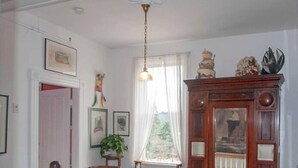 Una escalera con barandilla de madera y balaustres blancos, que conduce a una habitación con un mueble de madera grande, una ventana con cortinas translúcidas y obras de arte enmarcadas en las paredes.