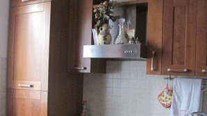 Een keuken met houten kastjes, een gasfornuis, een spoelbak en een eettafel met stoelen.