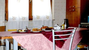 Een eetruimte met een tafel voor vier personen, voorzien van een roze tafelkleed en bloemrijk gestoffeerde stoelen.