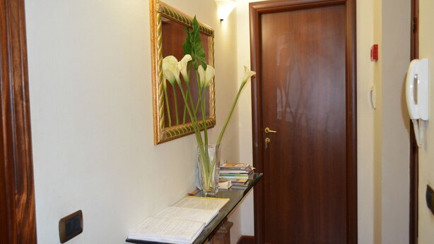 Een hal met een houten deur, een spiegel met gouden lijst en een vaas met witte bloemen op een consoletafel.