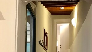 Un couloir étroit, avec une porte en verre sur la gauche, un escalier en bois au centre et une porte blanche au fond.