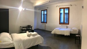 Une chambre avec deux lits, un bureau et deux chaises. Elle comporte deux fenêtres équipées de volets.