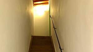 Un escalier en bois, doté d’une rampe, mène à une pièce où se trouve un luminaire au sommet.