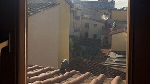 Une vue depuis une fenêtre donnant sur des toits recouverts de tuiles en terre cuite et sur un bâtiment historique doté d’un dôme et d’une tour.