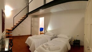Une chambre d’hôtel avec deux lits, une table en verre et un escalier.