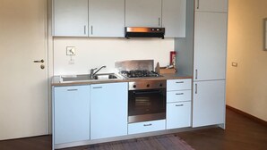 Une cuisine compacte avec des meubles blancs, une cuisinière à gaz, un four encastré et un petit évier.