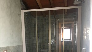 Une salle de bain avec une douche à parois de verre, deux toilettes, un lavabo blanc et un radiateur.