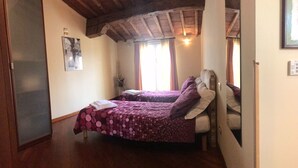 Une chambre avec deux lits, des poutres en bois au plafond, une fenêtre avec des rideaux et un tableau encadré au mur.