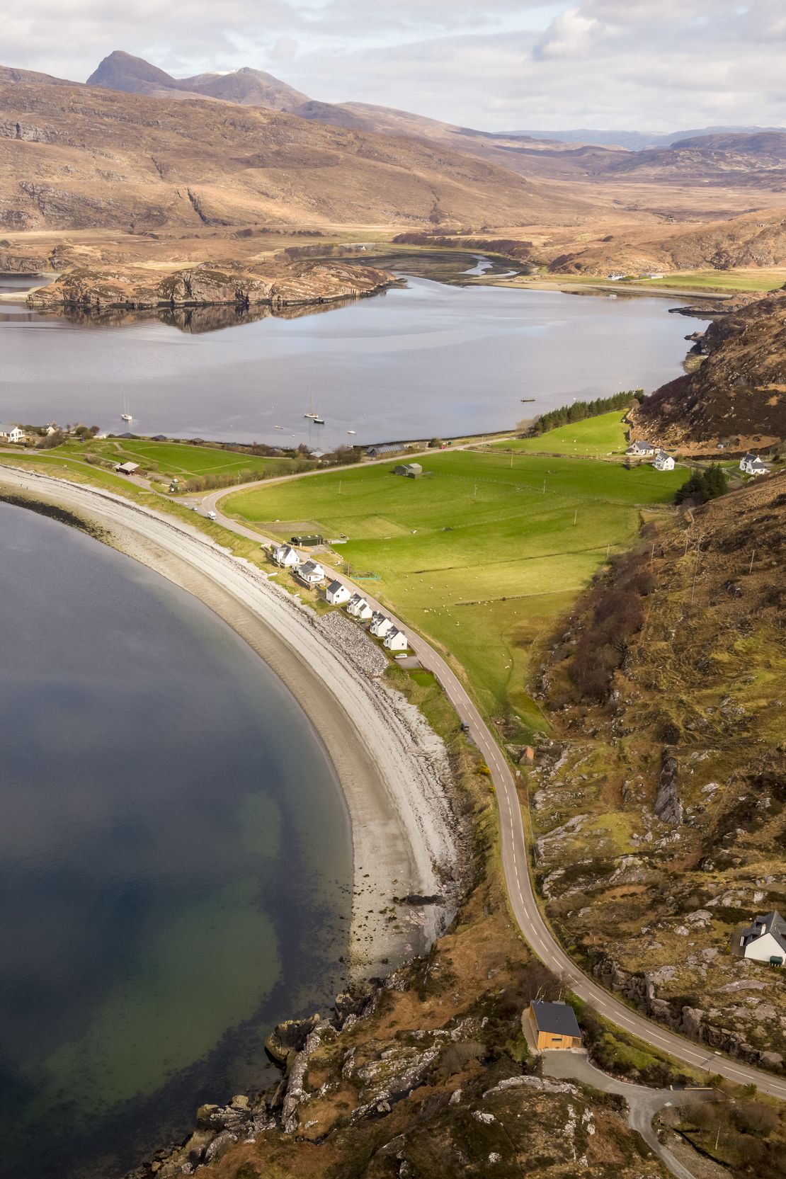 A coastal landscape with a road curving along the shore, a small settlement with houses, and a large body of water.
