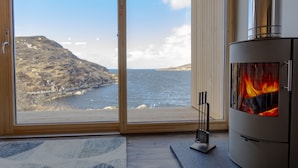 Une pièce dotée d’une grande fenêtre donnant sur un paysage côtier, d’une cheminée moderne et d’un plancher en bois.