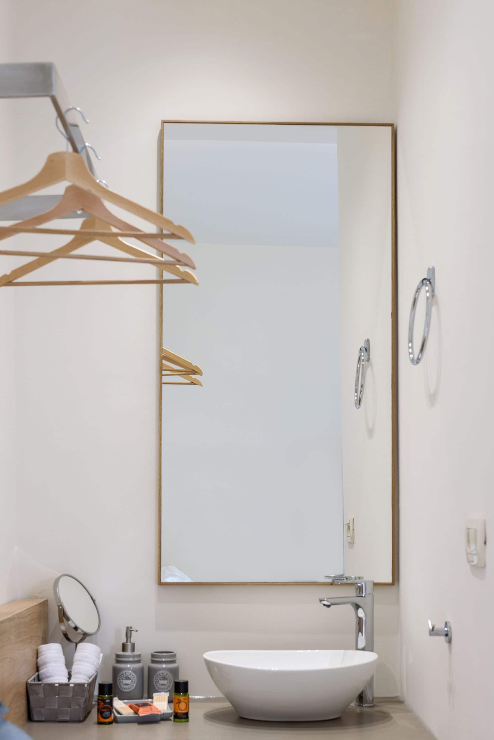 A modern bathroom with a large mirror, a white sink, and a towel rack.