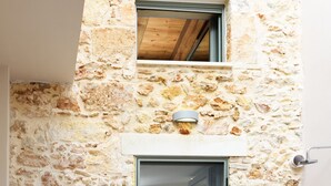 Ein Sitzbereich im Freien mit Steinwänden, zwei Stühlen und einem Tisch, einer Glastür sowie einem kleinen Fenster darüber.